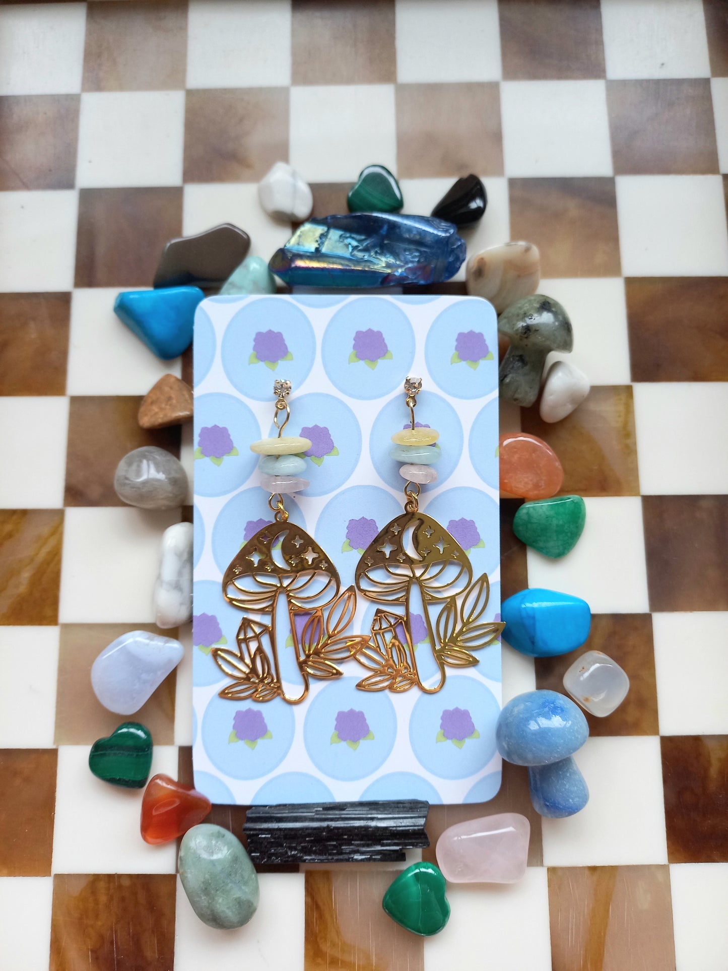 Pair of gold earrings on a card with decorative stones on a checkered background
