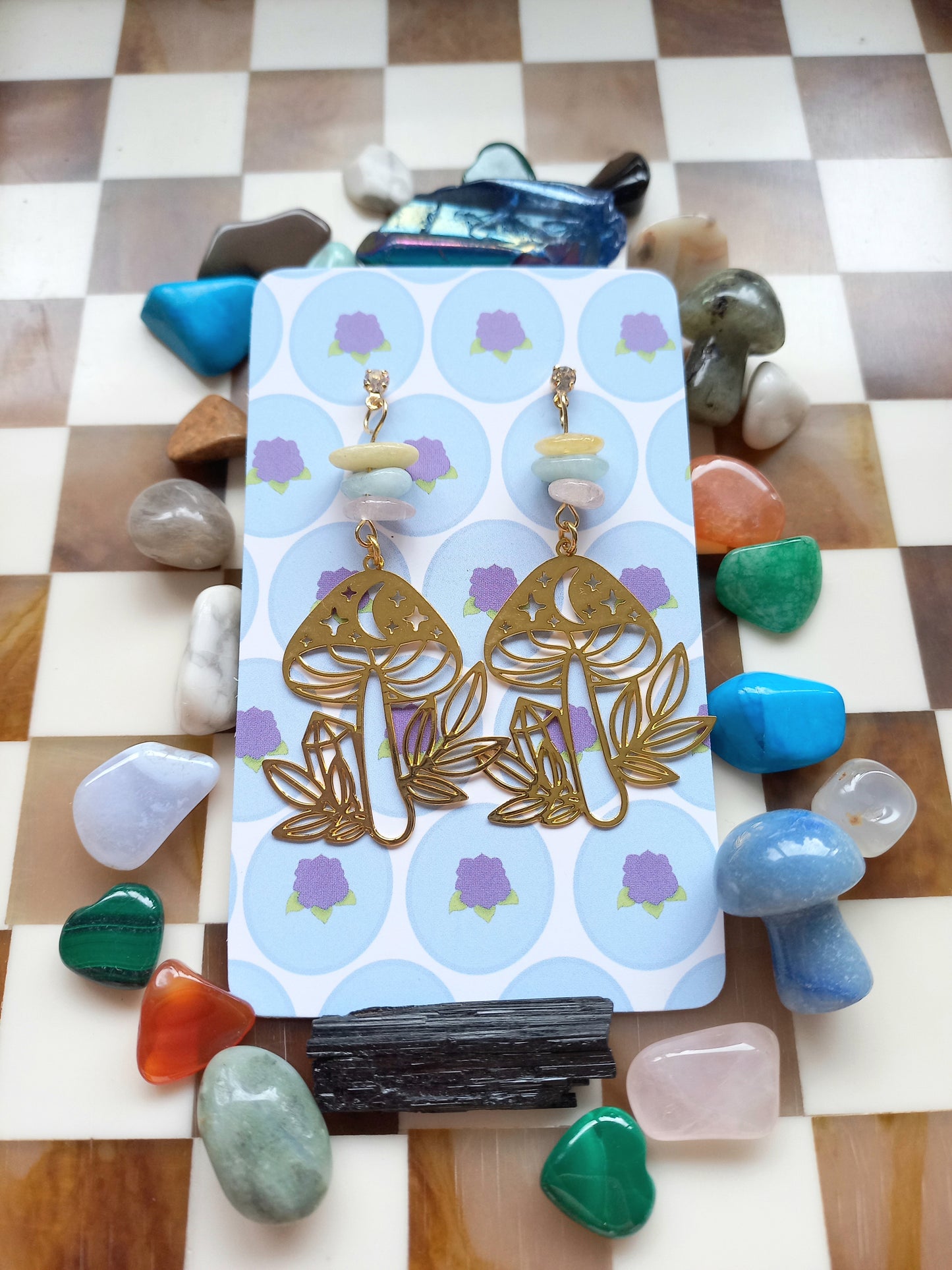 Gold earrings on a card with stones around on a checkered surface